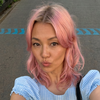 Person with pink hair taking a selfie on a street